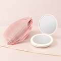 Blush pink velvet drawstring pouch beside an open white LED compact mirror with its light ring on and touch button visible