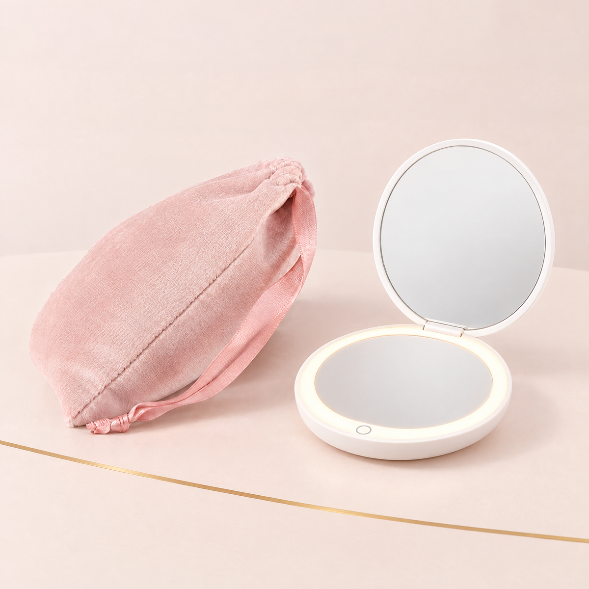 Blush pink velvet drawstring pouch beside an open white LED compact mirror with its light ring on and touch button visible