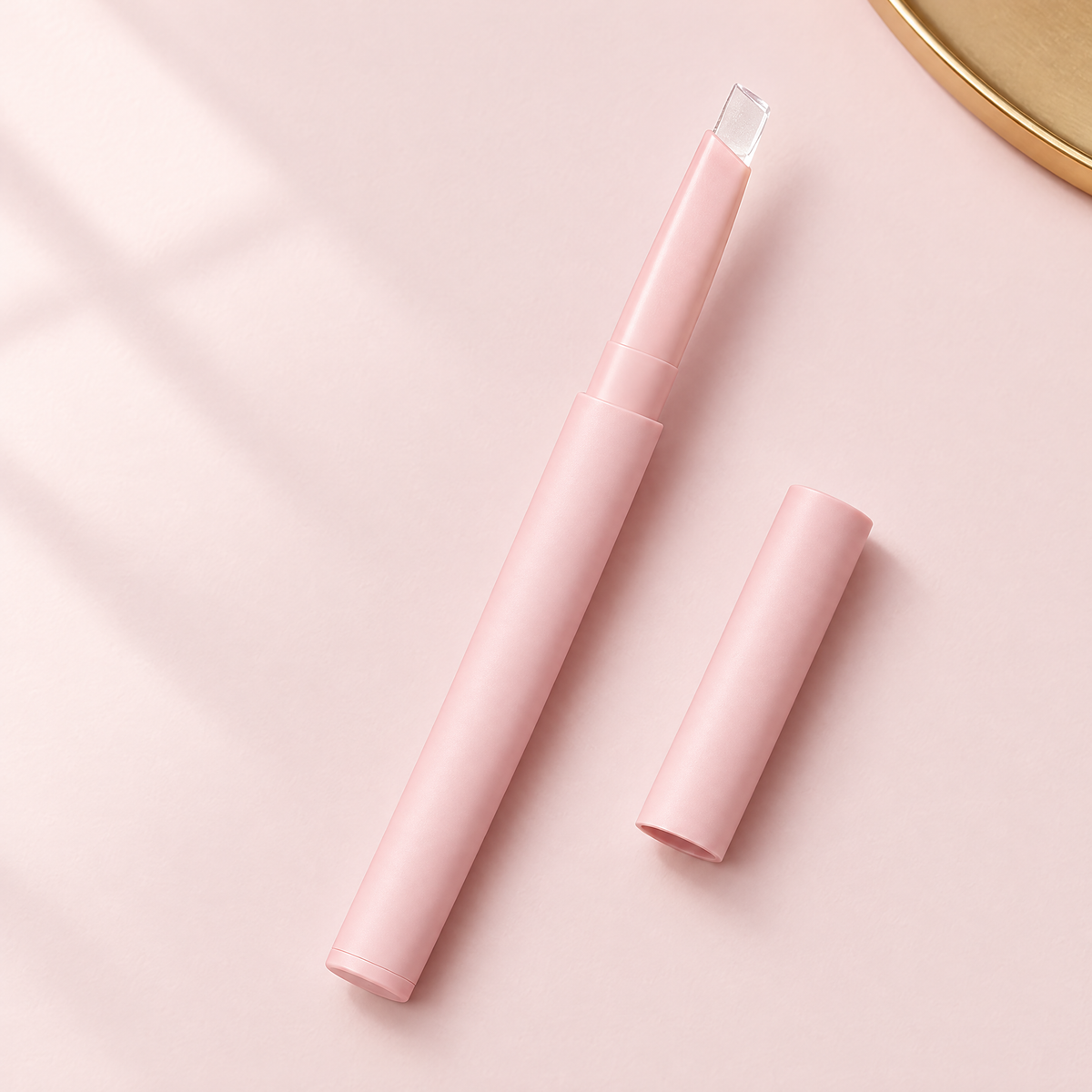 Clear twist-up lip liner pen with blush pink barrel and transparent tip, cap beside it, on a soft blush pink background